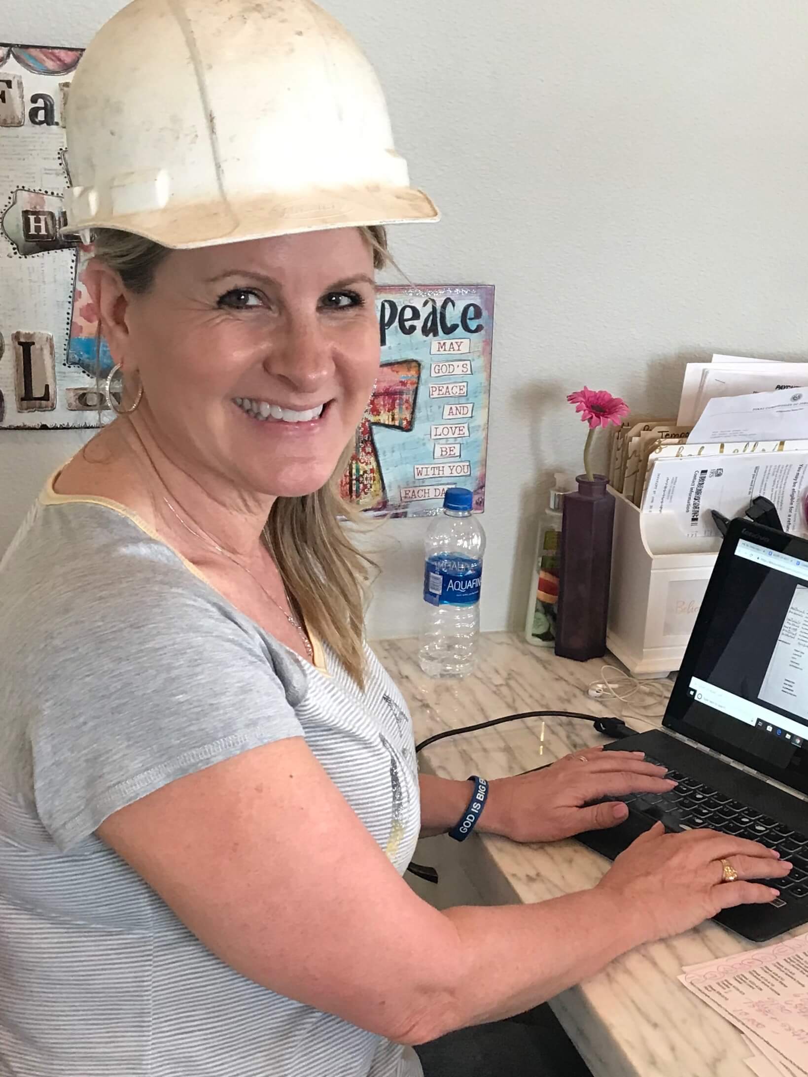 Lynda at her desk working on a computer and wearing a hard hat