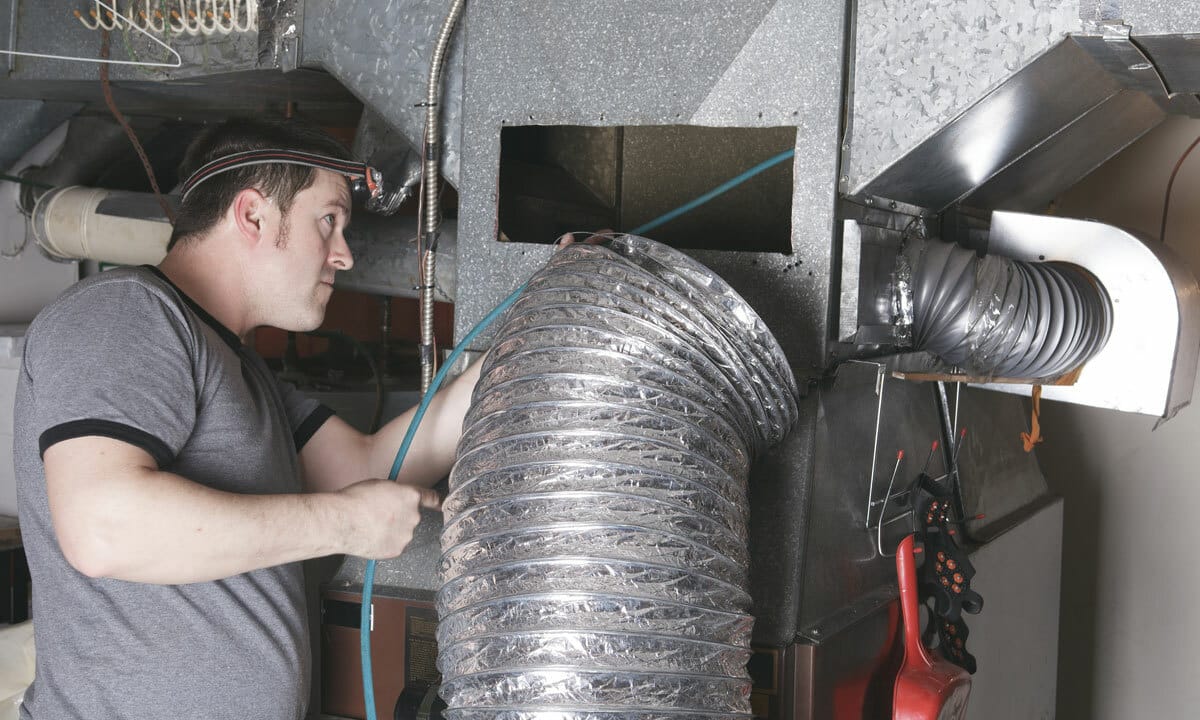 An HVAC technician adjusting system duct work in an attic