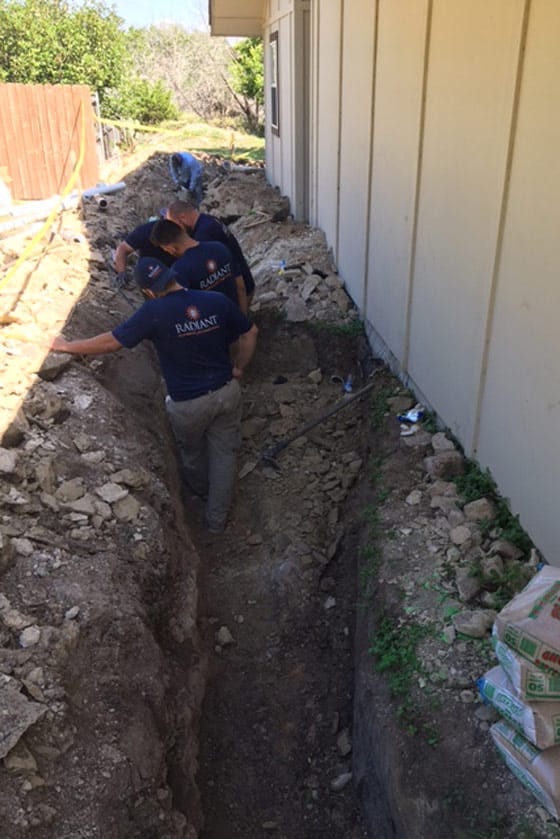 Radiant technicians in a trench replacing a sewer line at a home