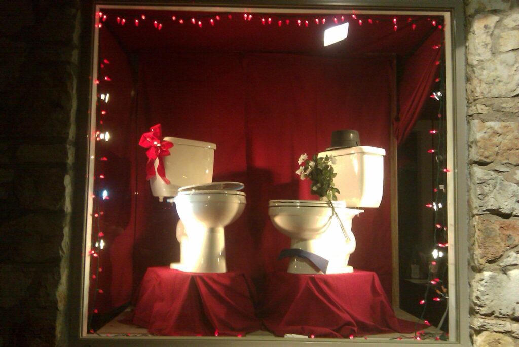 Toilet display at Radiant Austin office with a red background, two toilets with one in a hat and with flowers in the bowl