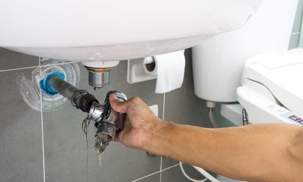 A person removing the sink drain pipe to remove a hair clog