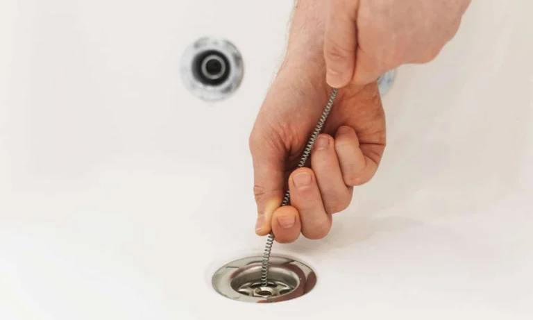 Up close photo of someone using a plumbers snake in a bathtub drain
