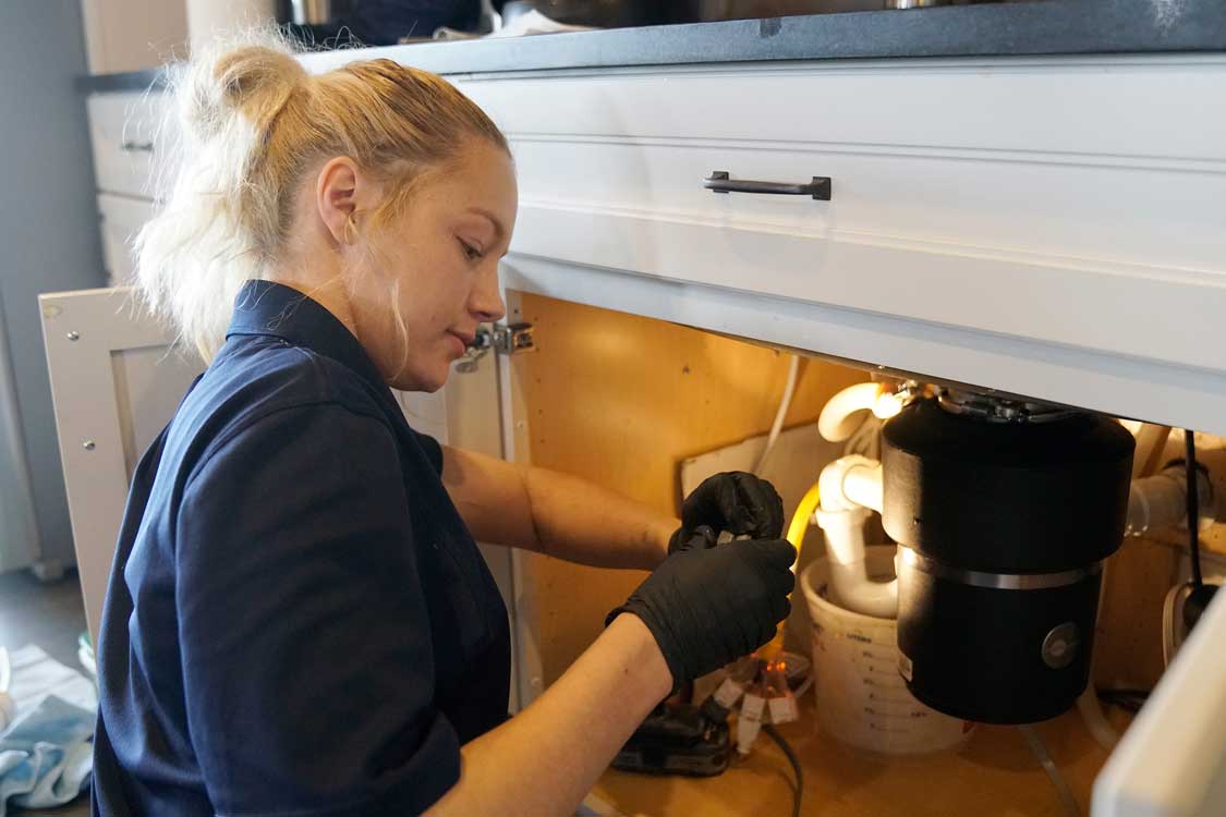 Plumber repairs a garbage disposal in a kitchen