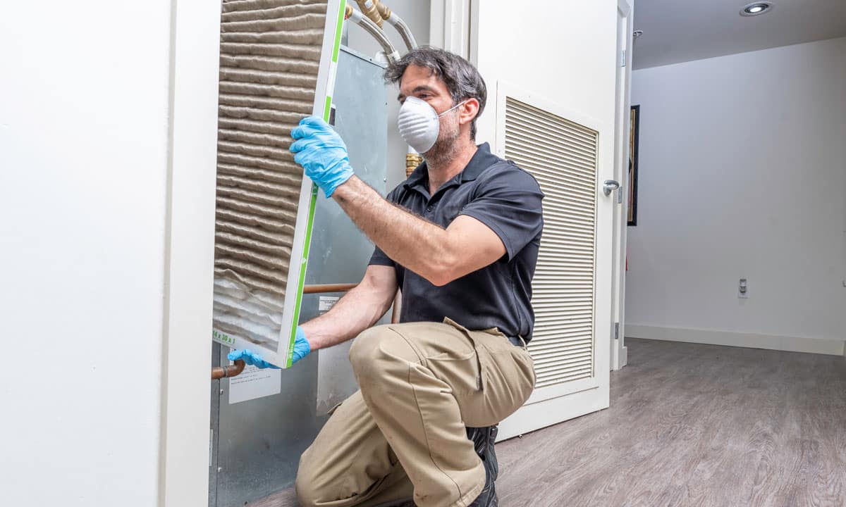 A person wearing protective gear to change a dirty air filter in a home.