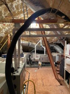Attic view of multiple HVAC systems, new ductwork, and updated PVC drain lines after installation.