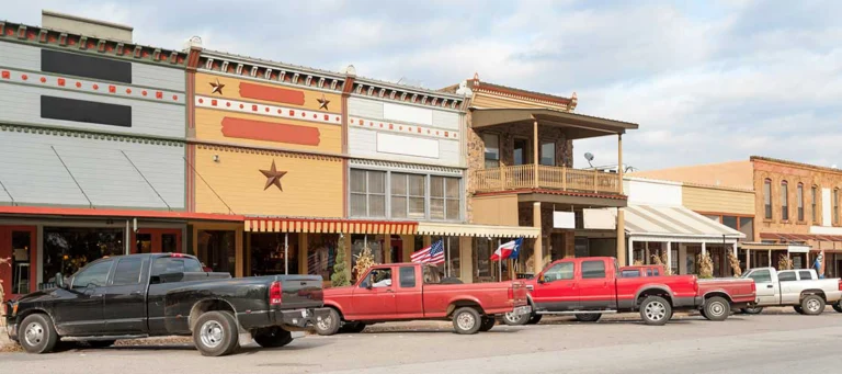 Old trucks with Texas flags parked on the street outside businesses
