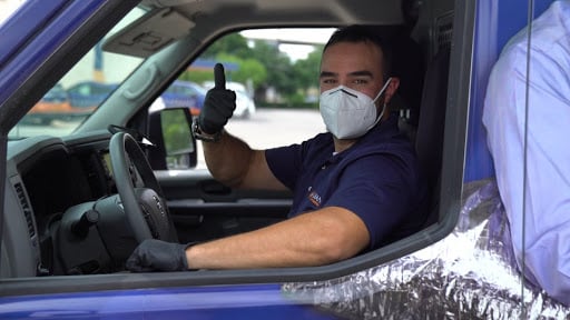 Radiant technician giving the thumbs up sign from his truck, while wearing a surgical face mask for protection from covid