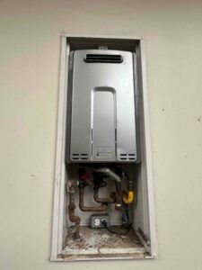 older exterior-mounted tankless water heater with aging piping and fittings
