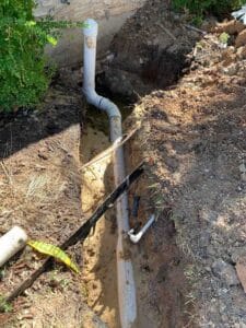 A newly installed PVC yardline (large white pipe) running through the trench.